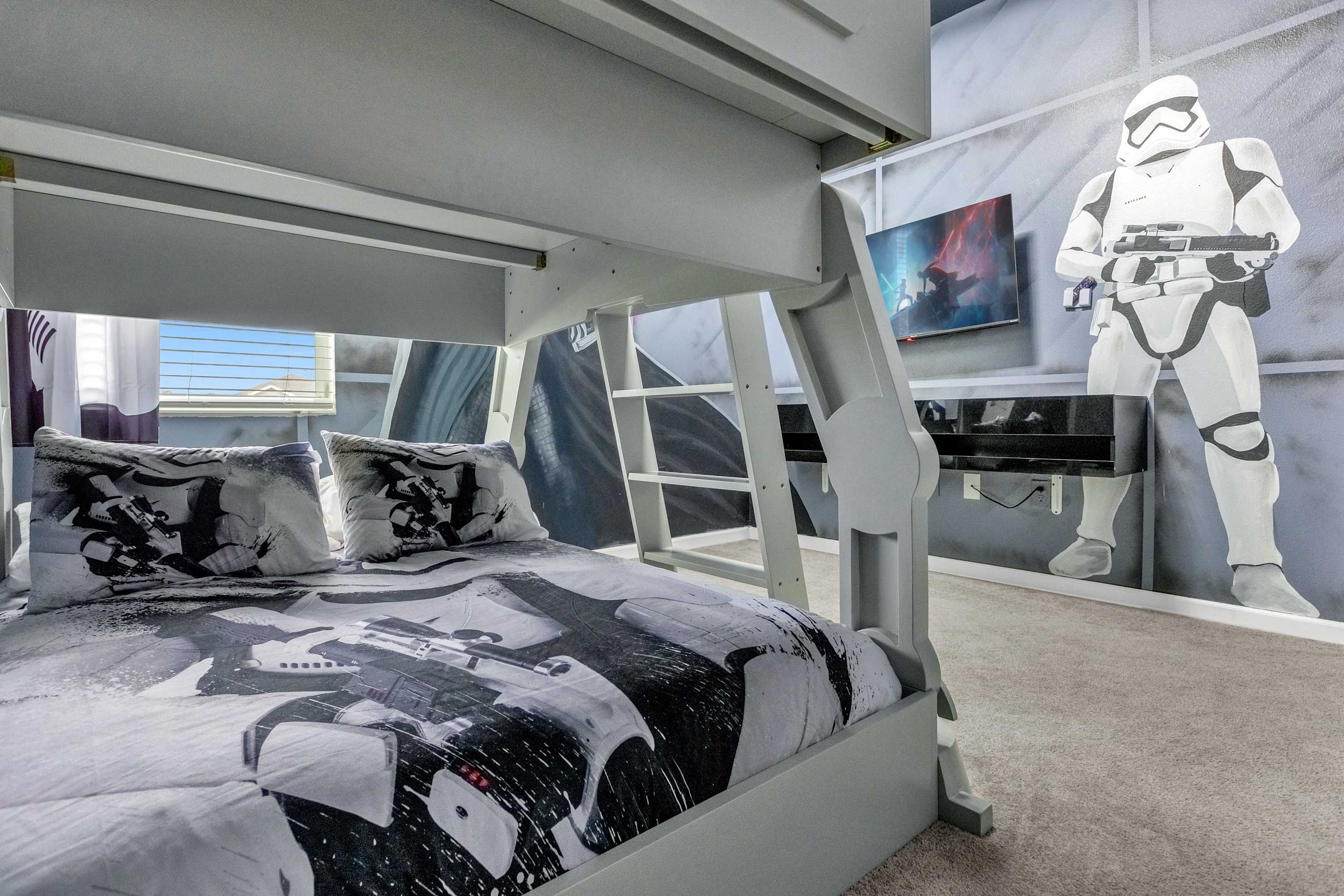 Another view of the Star Wars-themed bedroom, showing the lower bunk bed with Star Wars bedding, a wall mural of a Stormtrooper holding a blaster, and a wall-mounted TV above a black floating console.
