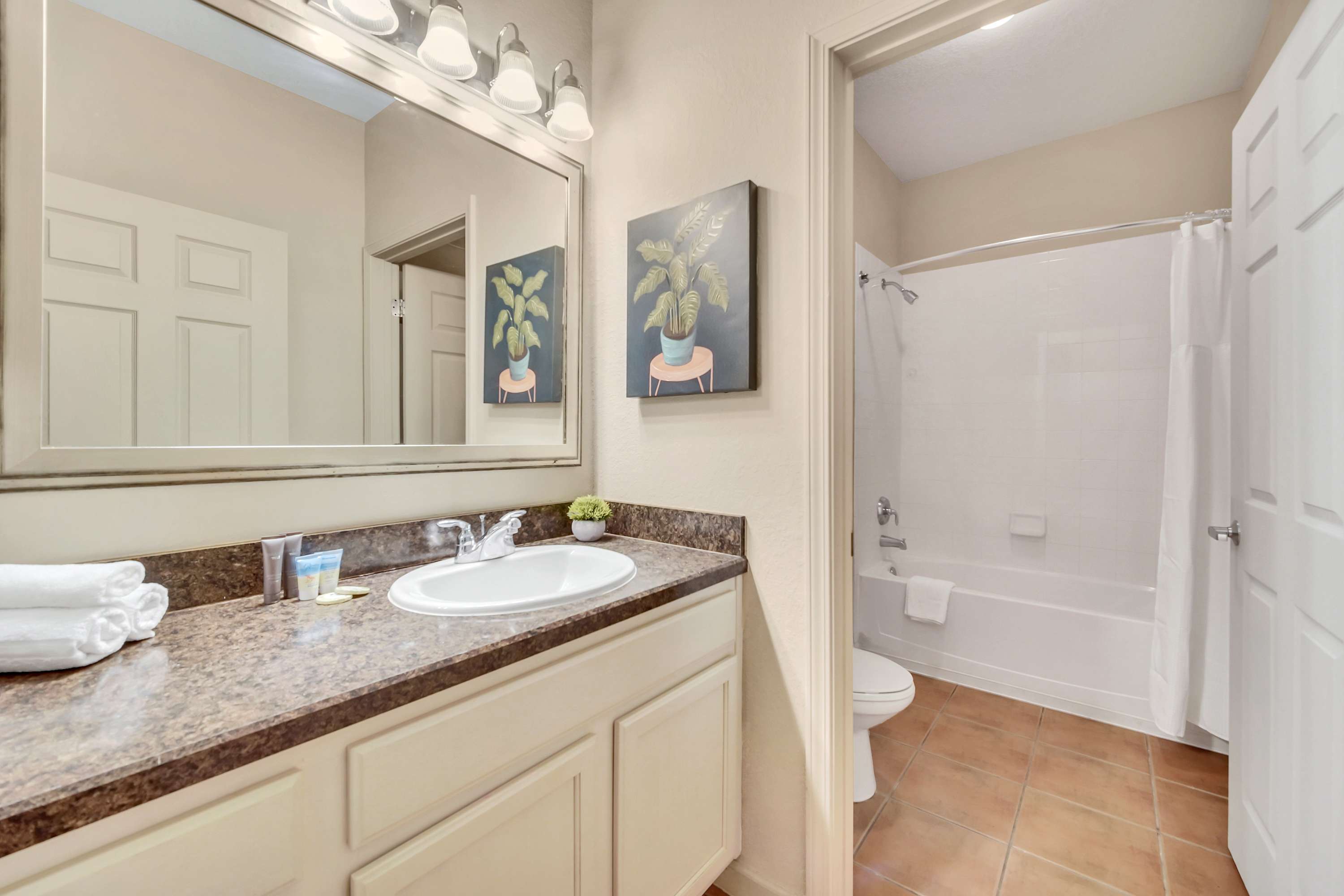 Bathroom with a single vanity featuring a brown speckled countertop, a large mirror with a multi-bulb light fixture, and a white shower/tub combination with a shower curtain.