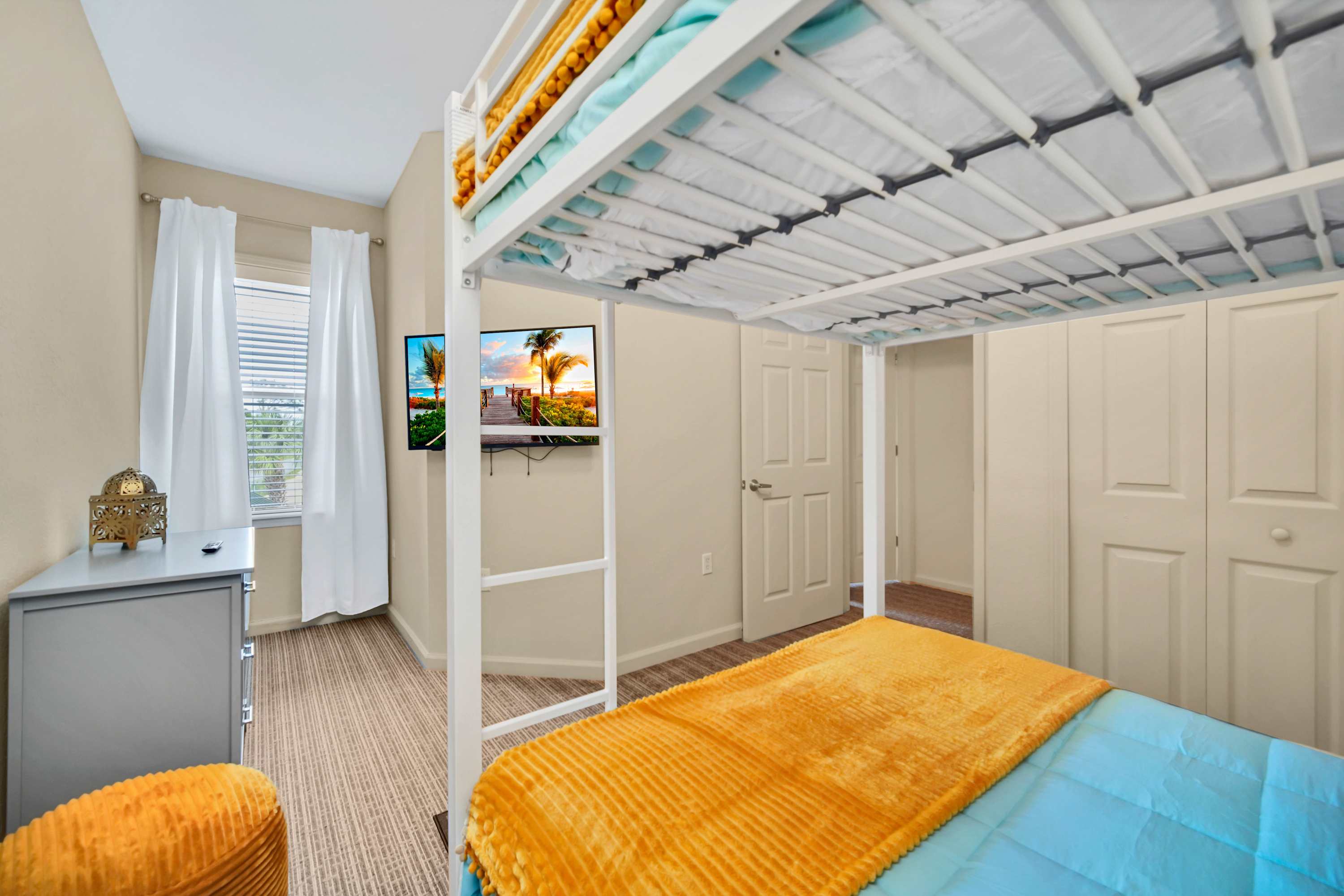 Another perspective of the kids' bedroom, showing the bunk beds, a window with white blinds and curtains, and a closet with bi-fold doors, offering additional storage.