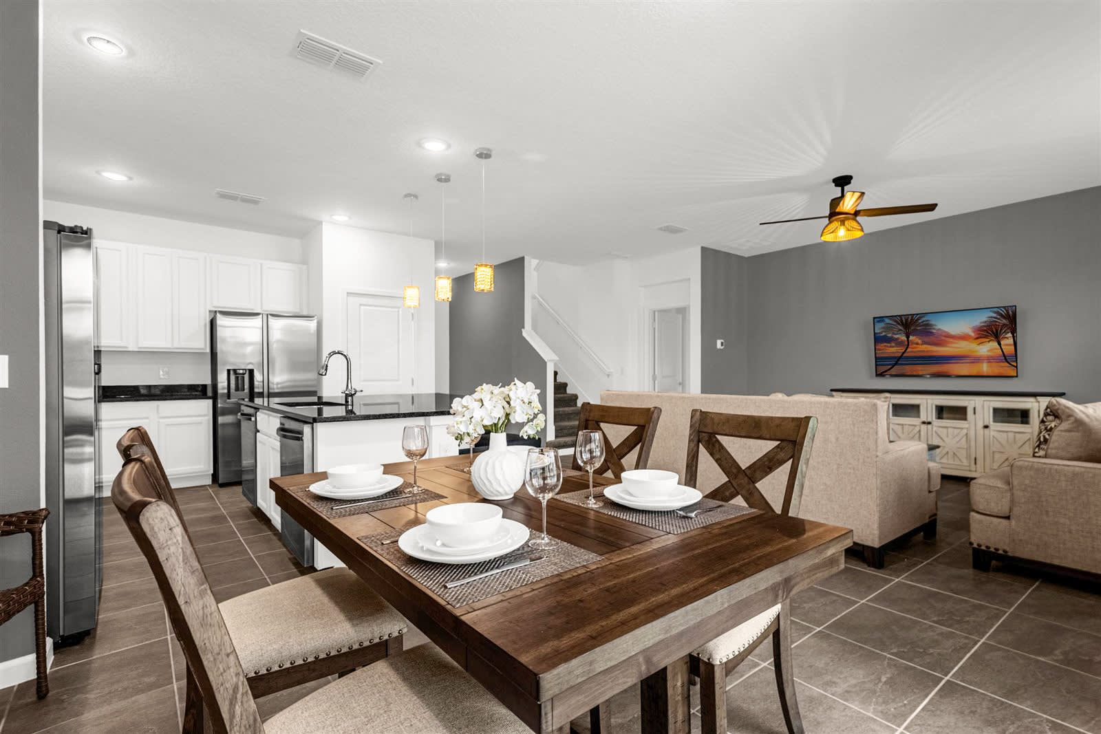 A modern kitchen with white shaker-style cabinets, black granite countertops, and stainless steel appliances, including a refrigerator and range. A kitchen island with pendant lighting provides additional counter space and seating, connecting to the open-concept dining and living areas.