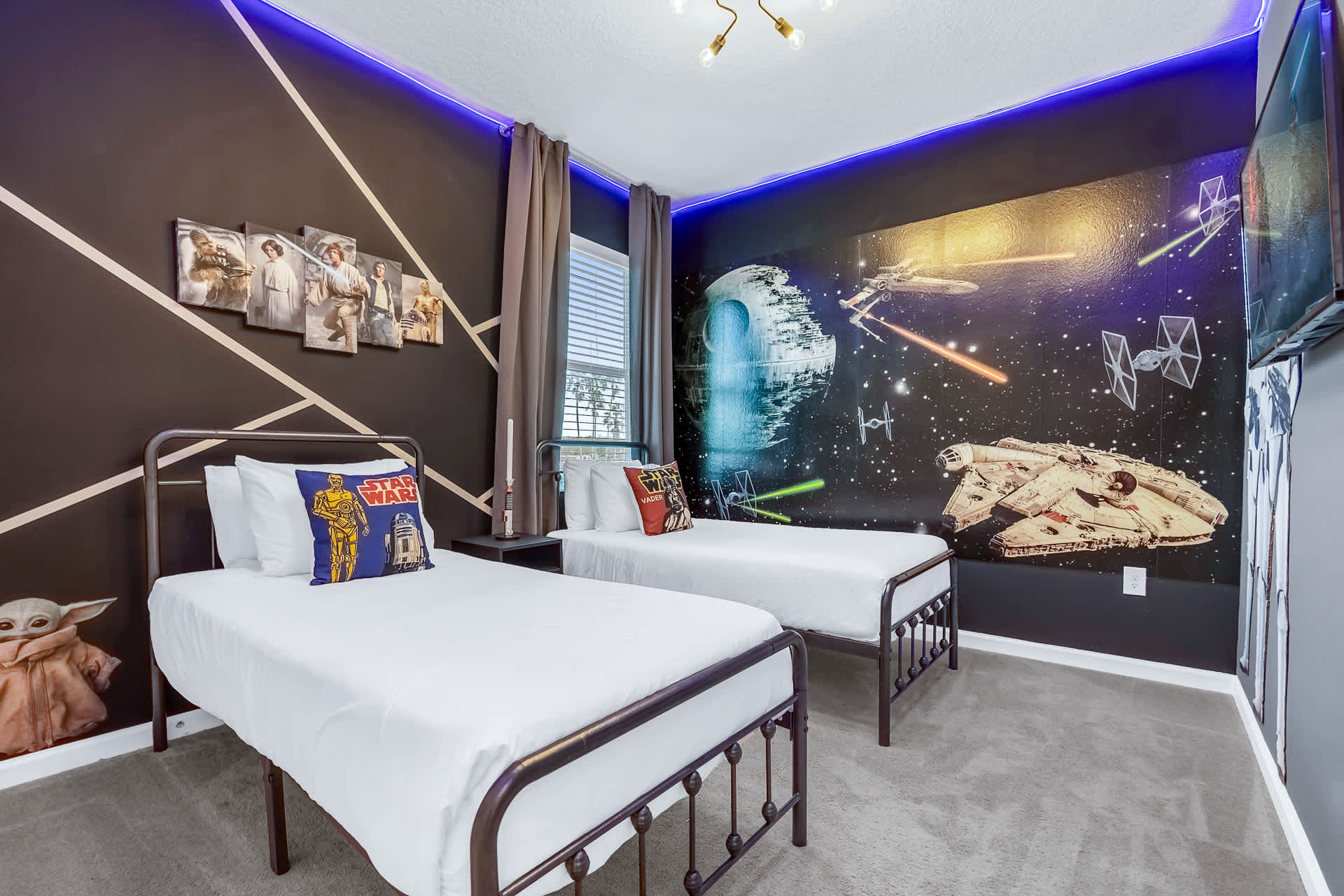 Star Wars themed bedroom featuring two twin beds with black metal frames and a dramatic mural of the Death Star and Millennium Falcon. Blue LED strip lighting illuminates the dark walls, complemented by character artwork.