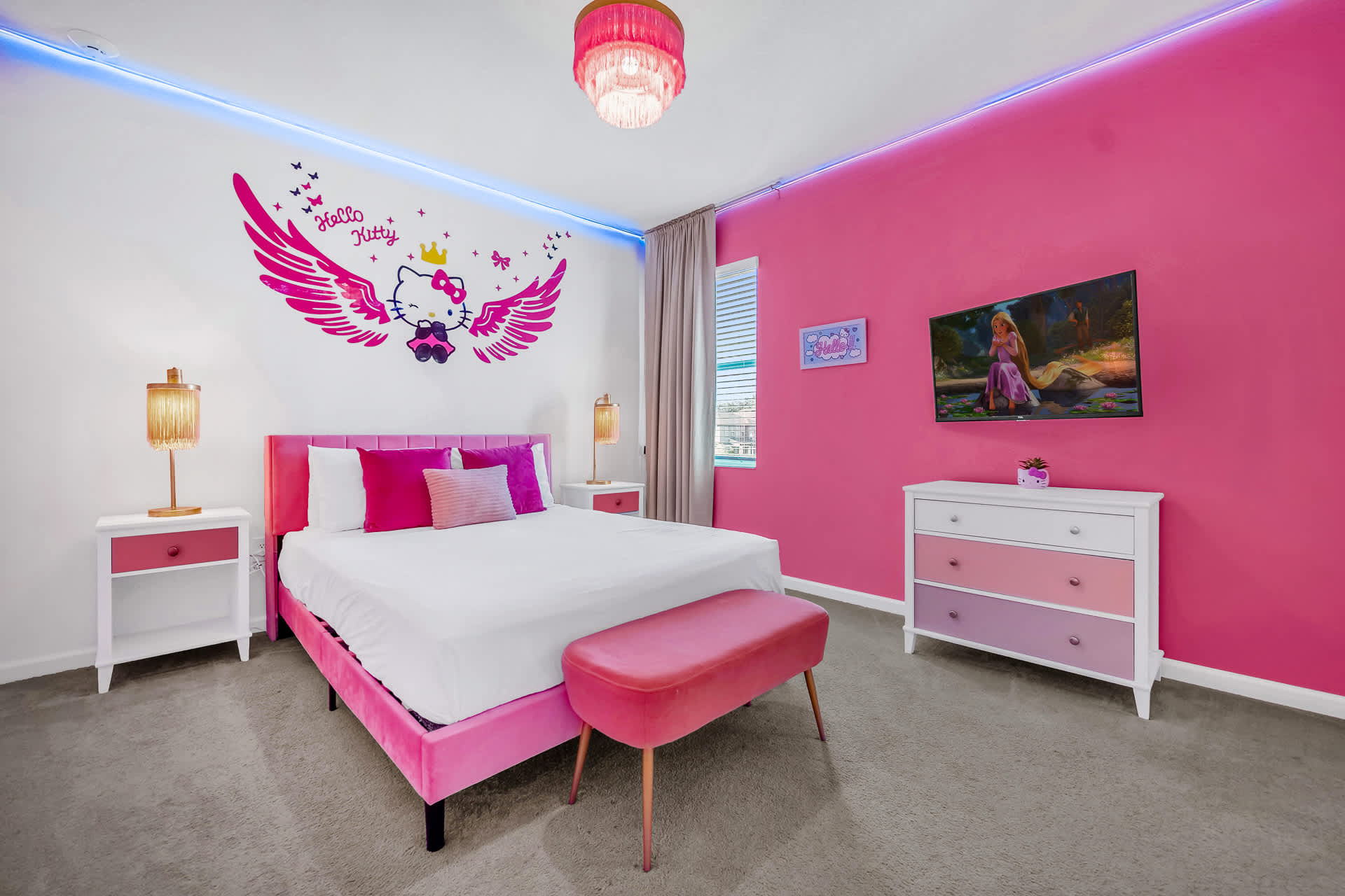 Vibrant Hello Kitty themed bedroom with a pink velvet queen bed, matching bench, and nightstands. The room features a large Hello Kitty wall decal, bright pink accent wall, and blue LED strip lighting along the ceiling.