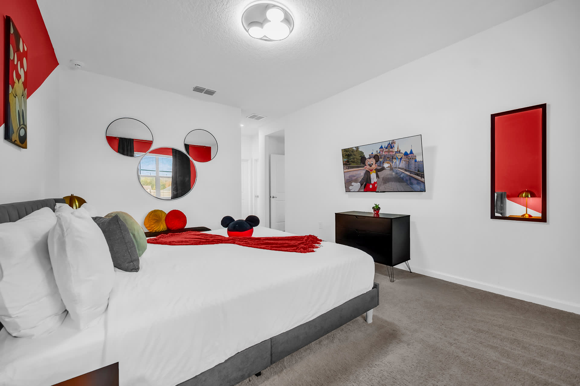 Another view of the Mickey Mouse themed bedroom, featuring a large bed with themed pillows, a wall-mounted TV, and a unique Mickey-shaped mirror arrangement.