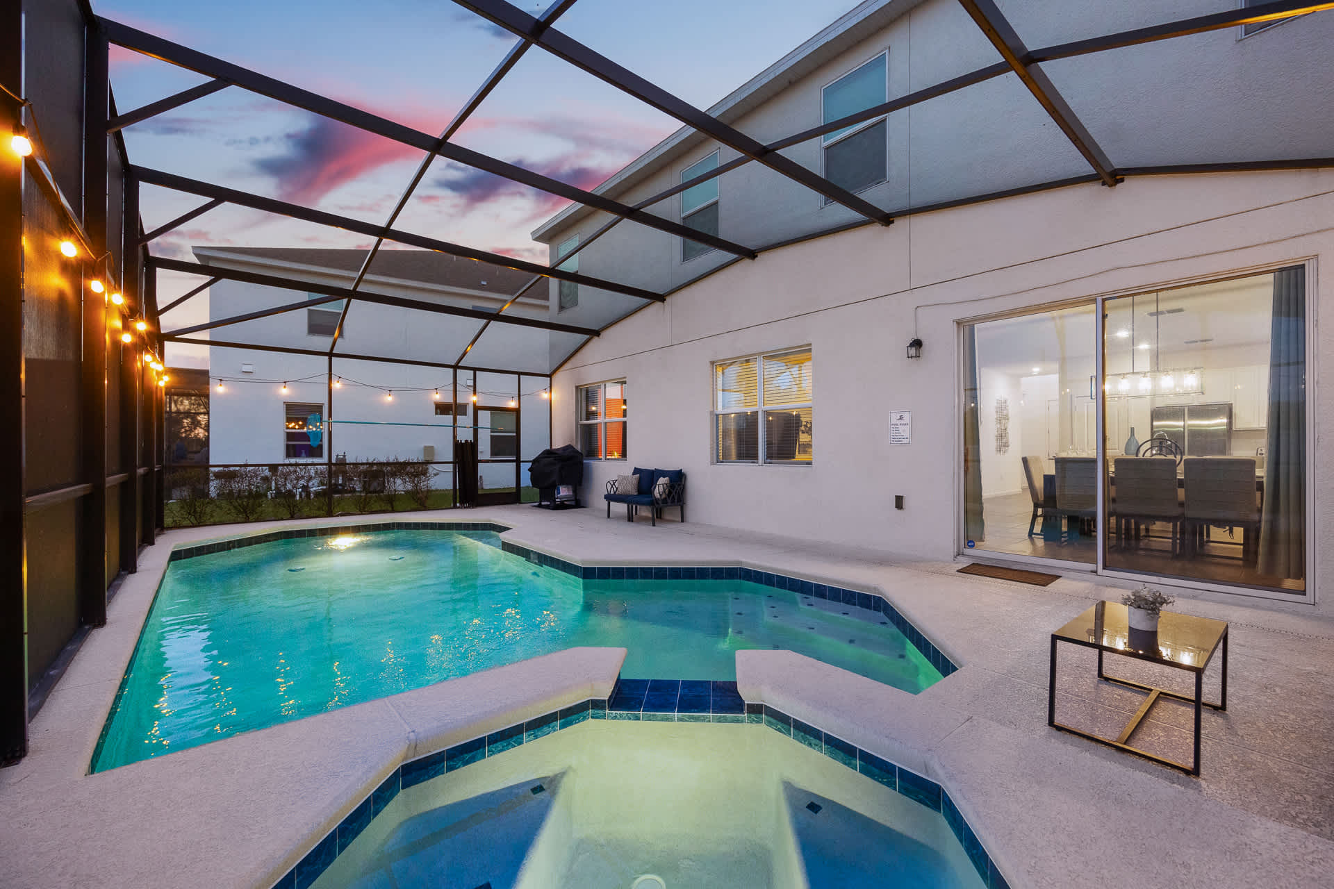 The back exterior of the house featuring a screened-in pool area with a swimming pool and hot tub, a BBQ grill, and outdoor seating, with sliding glass doors leading into the dining area.