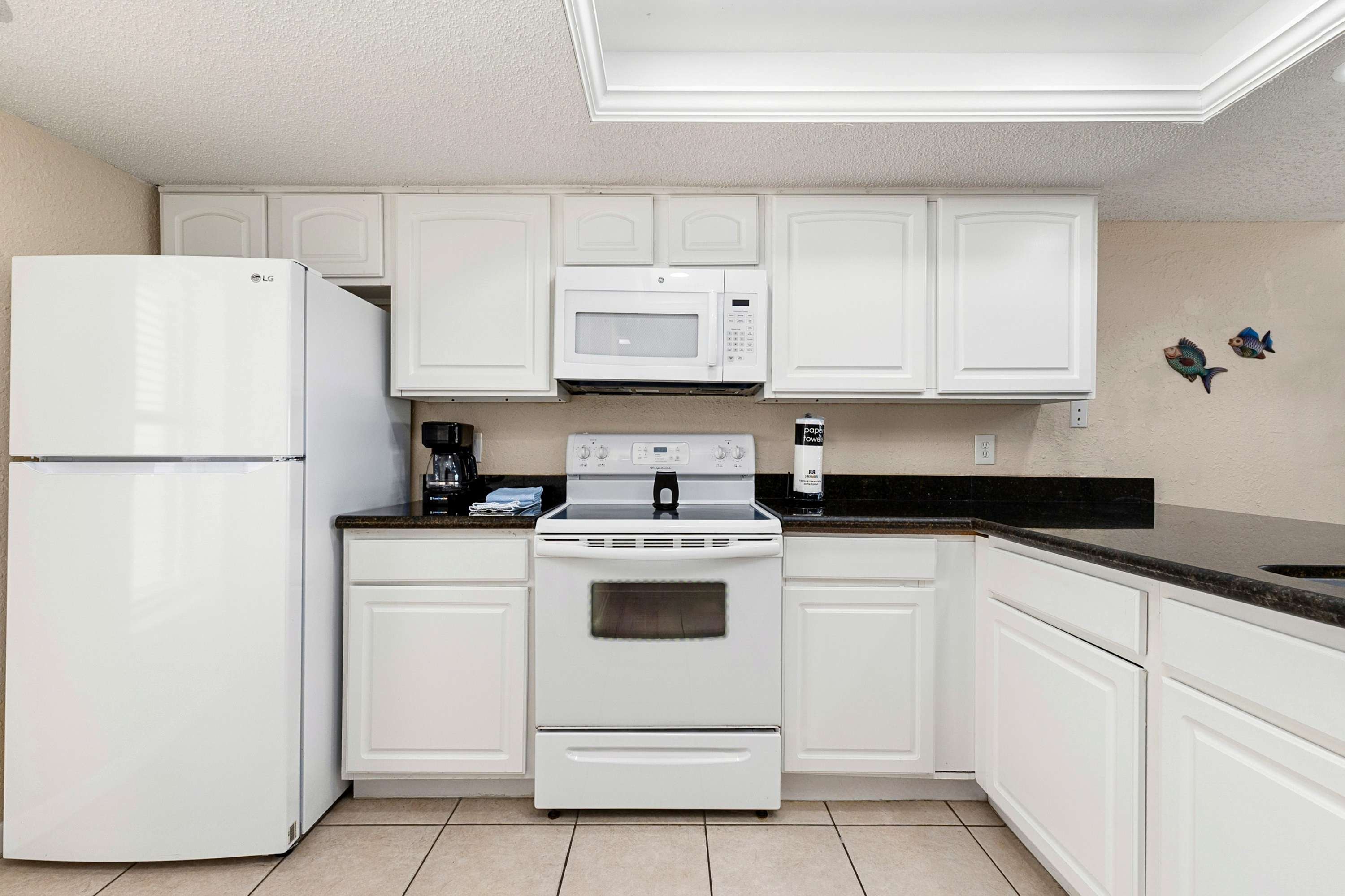 Kitchen area with a double sink set into black granite countertops, white cabinetry, and a white dishwasher, offering a view into the open-concept living and dining space.