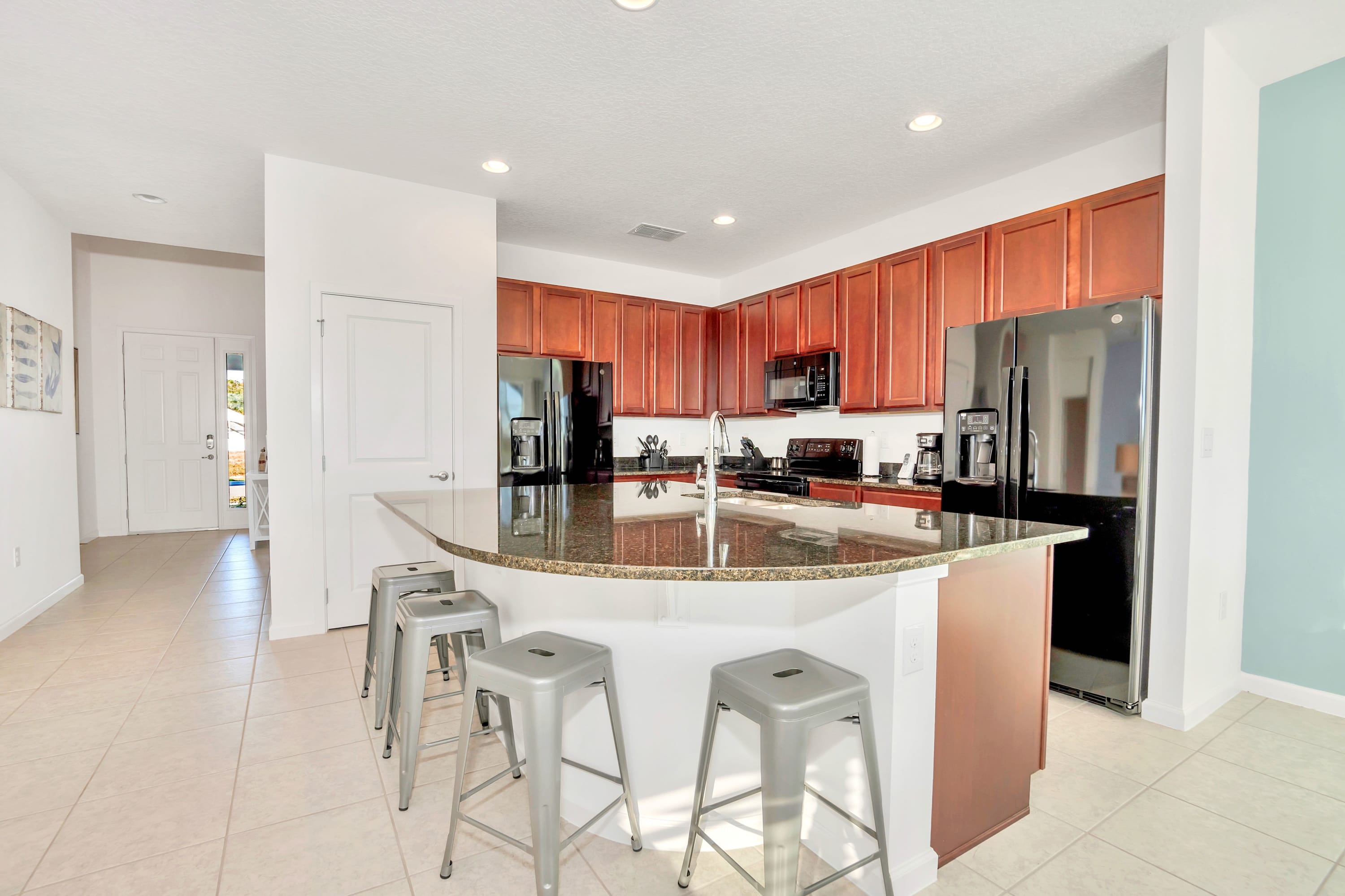 Spacious kitchen featuring extensive dark wood cabinets, black appliances, and a large granite island with bar seating, with a doorway leading to the front entrance area.