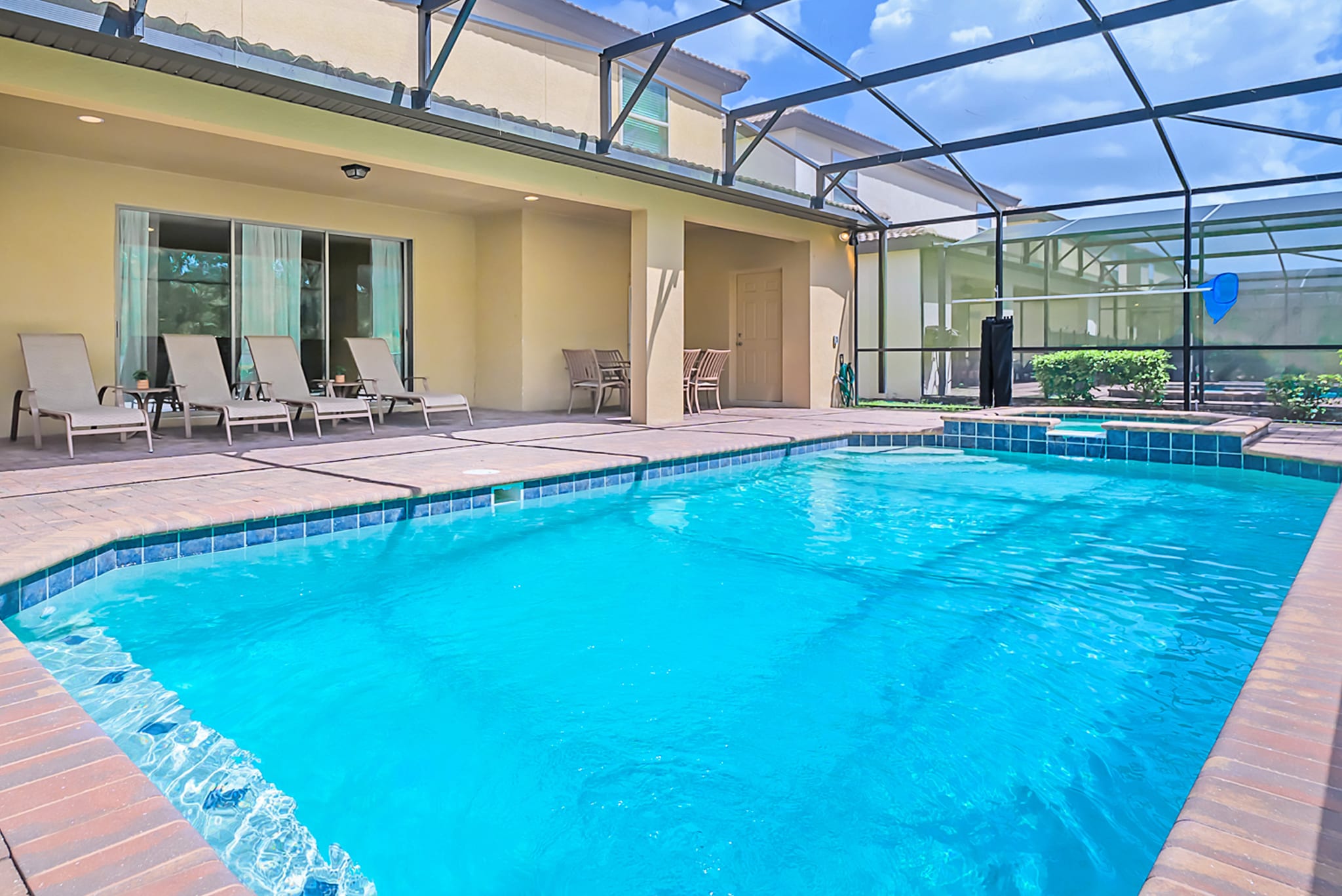 Screened-in private swimming pool area with a rectangular pool, surrounded by brick pavers and several lounge chairs, offering a view of the house's exterior and a covered patio.