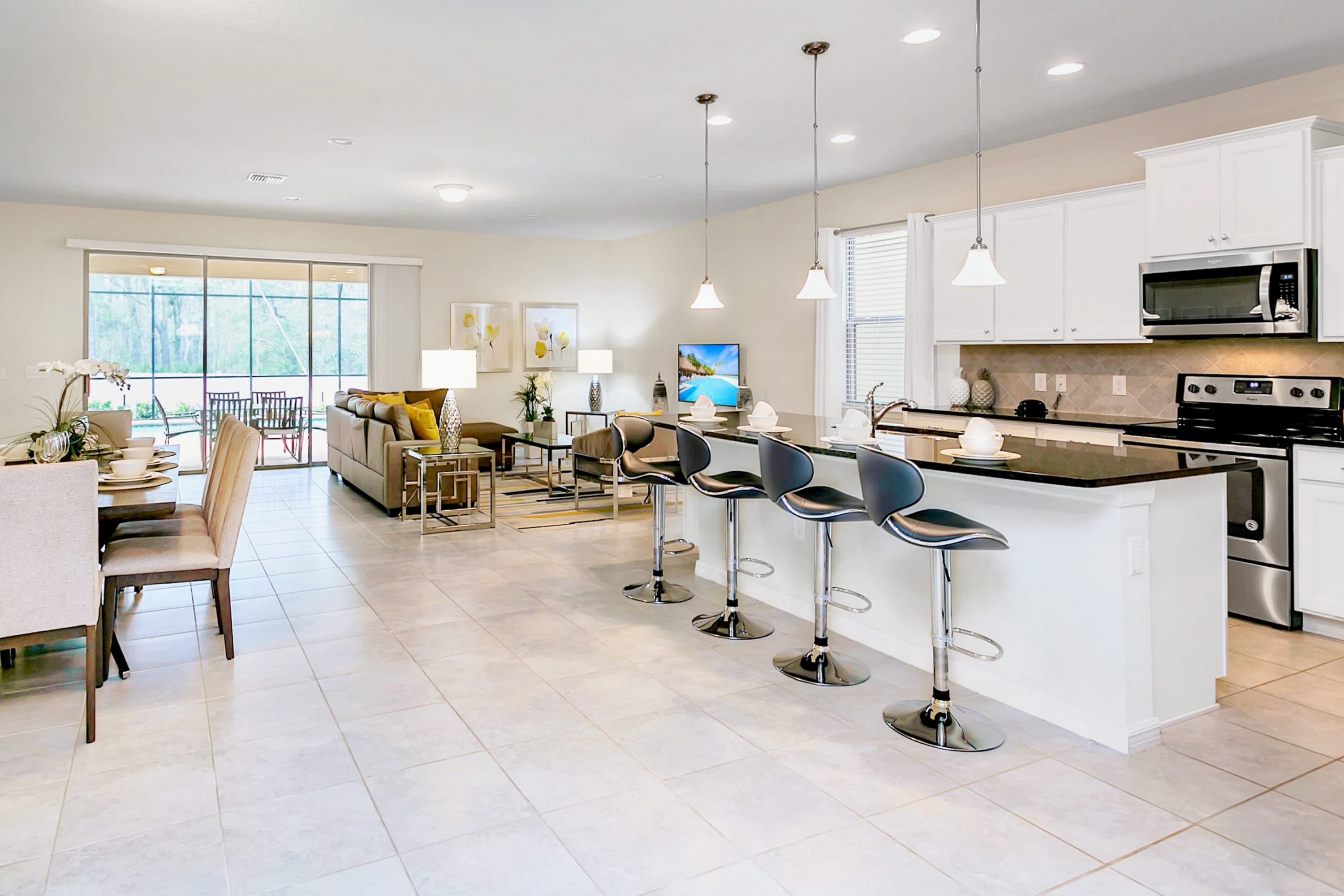 Expansive open-concept living area showcasing a modern kitchen island with bar seating, leading into a comfortable living room with a sofa and a dining area. Sliding glass doors open to an outdoor space.