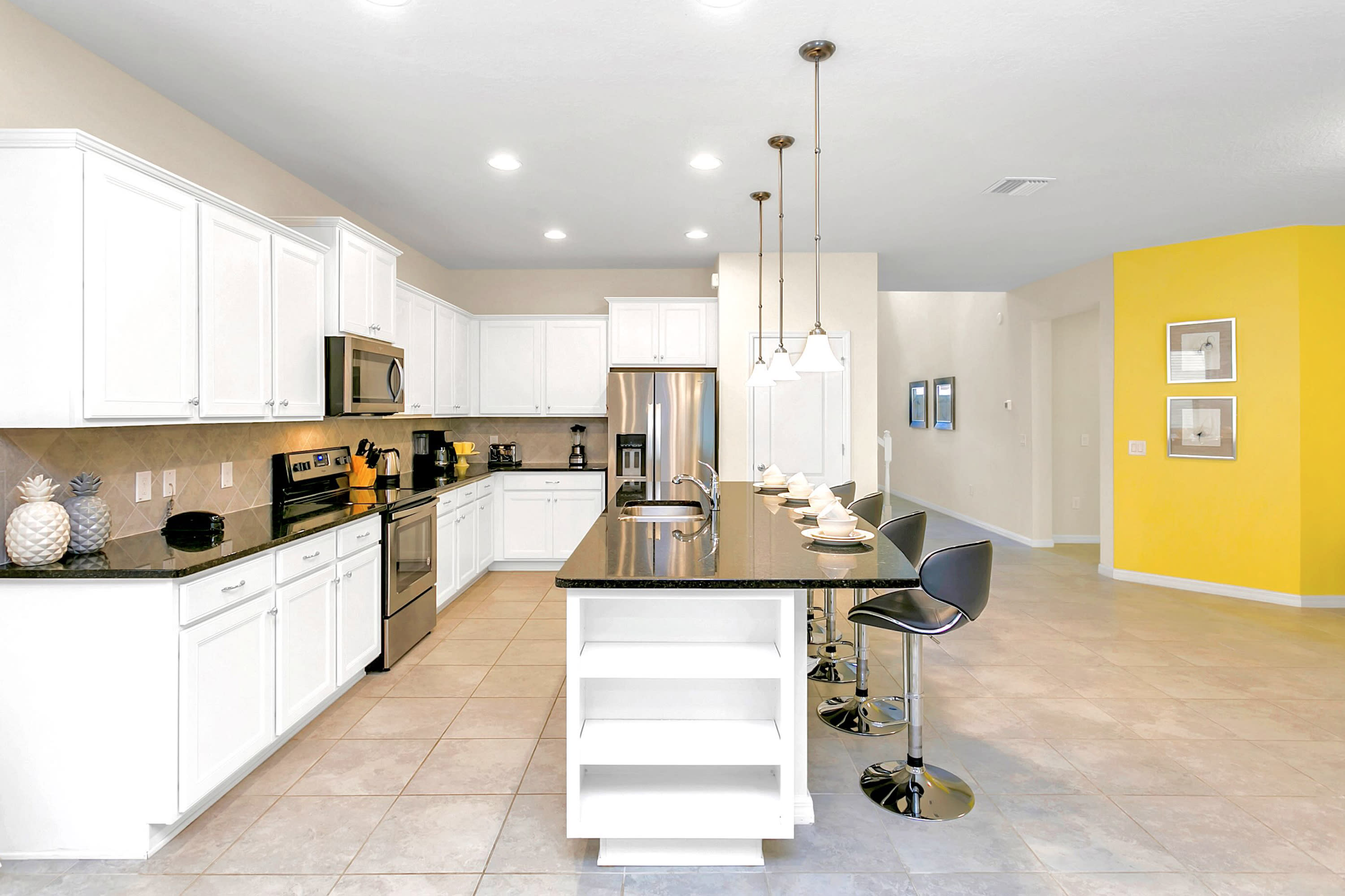 Contemporary kitchen with white shaker-style cabinets, black granite countertops, and stainless steel appliances including a microwave, range, and refrigerator. A large island features a sink, pendant lighting, and seating for four.