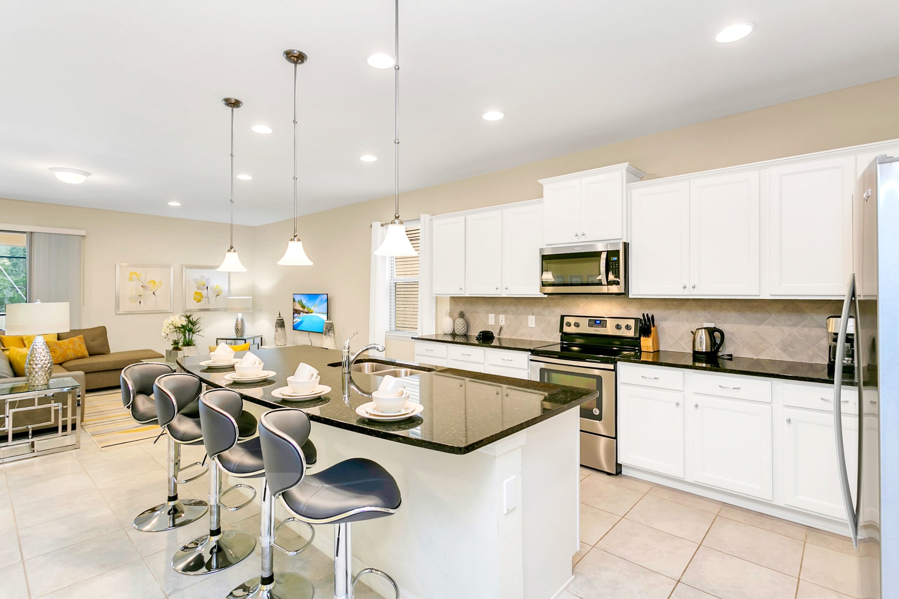 Well-appointed kitchen featuring white shaker cabinets, black granite countertops, and stainless steel appliances. A large island with a sink and pendant lights is set with dishes, offering additional counter space and seating.